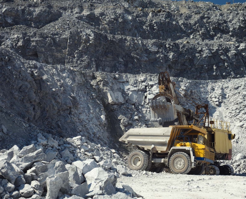 Mining excavator and heavy mining truck in a quarry for the extraction of limestone on the background of rocky terrain in sunny weathe