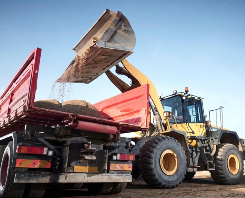 Image of an excavator loading sand onto a trailer truck.
